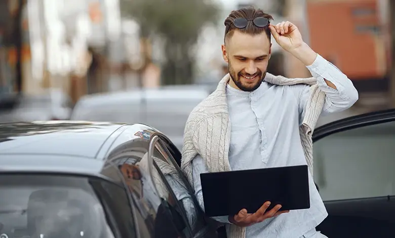 Smiling Man with Laptop Standing Next to a Car