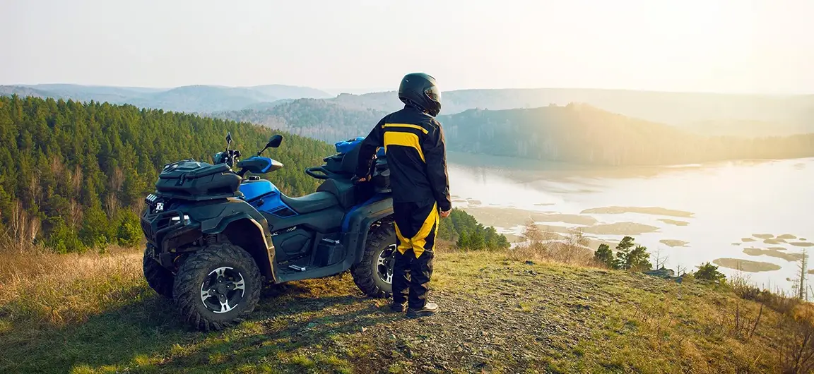 Person in Helmet Standing Next to ATV Overlooking Scenic Lake Landscape