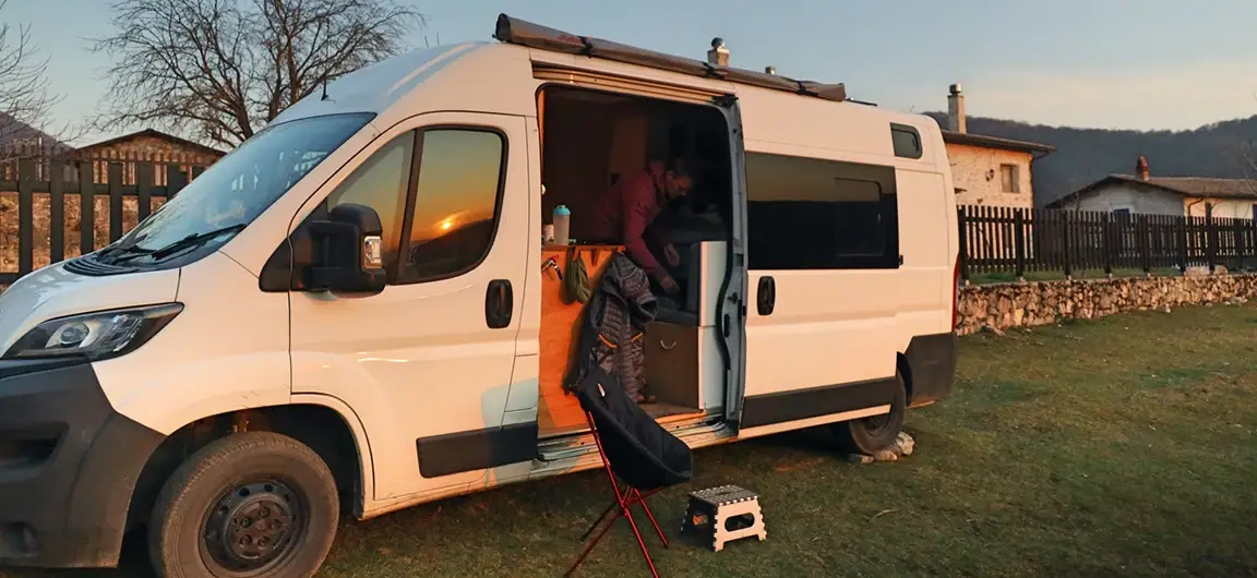 Person Preparing Meal Inside Camper Van Parked on Grass Field