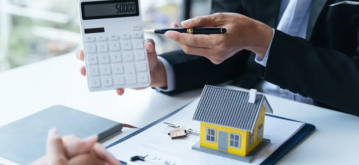 Businessperson Calculating Home Insurance Costs with Model House and Calculator