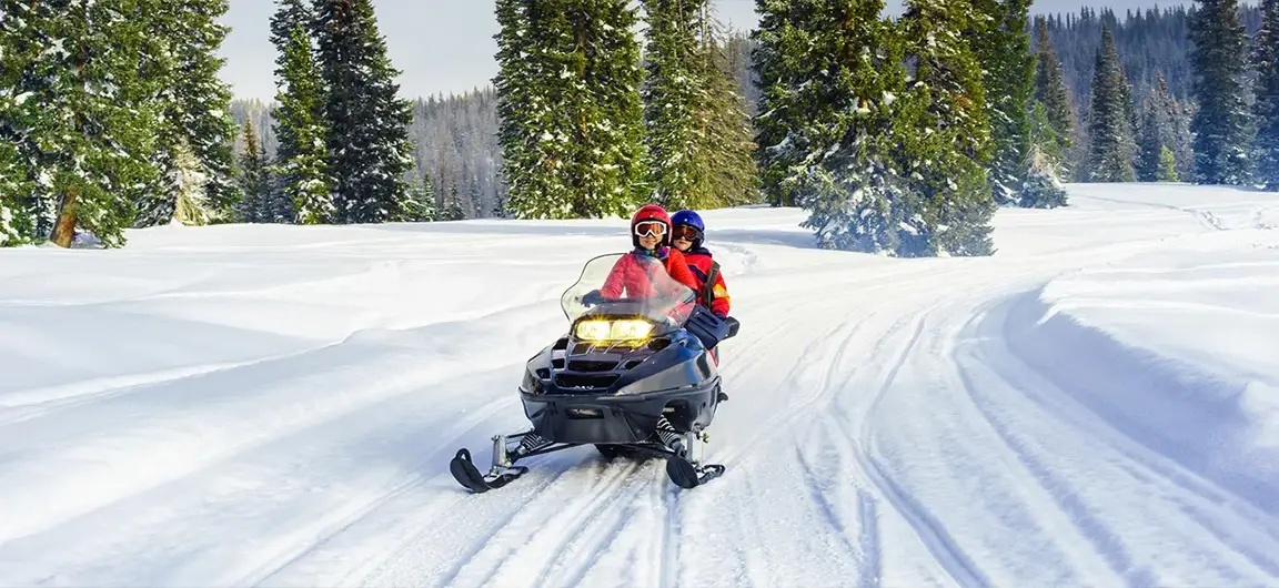 Two People Riding a Snowmobile Through Snowy Forest in White Bear Lake